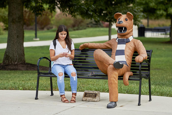 Student checks her phone while seated by Nittany Lion Mascot